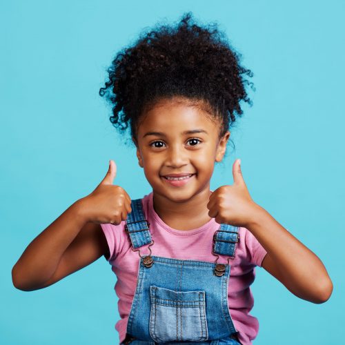 Shot of an adorable little girl showing thumbs up while standing against a blue background.